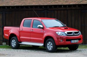 A 2009 Toyota Hilux midsize pickup truck model with a red paint color option parked on a dirt and gravel path