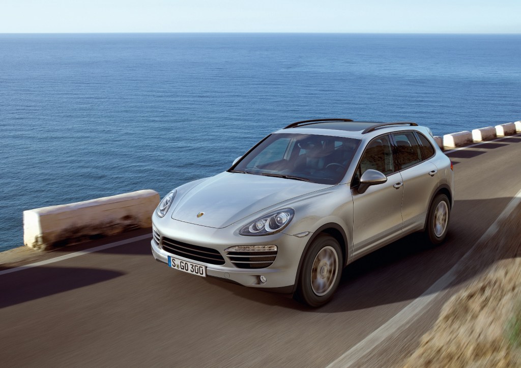 A silver 2011 '958' Porsche Cayenne driving down a road next to an ocean