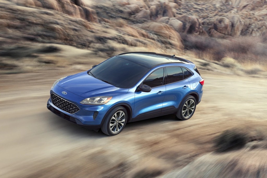 A blue 2021 Ford Escape drives along a dirt road, it's an affordable compact SUV.