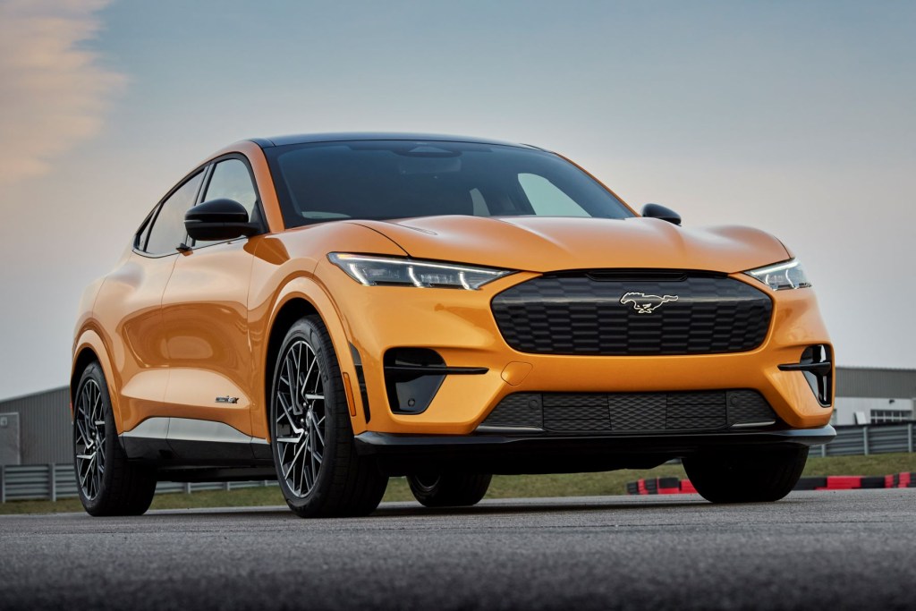 A 2021 Ford Mustang Mach-E GT all-electric compact SUV model with a gold color option parked on a race track.