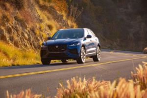 A blue 2021 Jaguar F-Pace driving through the mountain side surrounded by brown grass. 