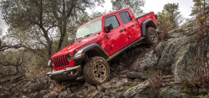A 2021 Jeep Gladiator midsize pickup truck with a red paint color option driving down a rocky cliff in the wilderness