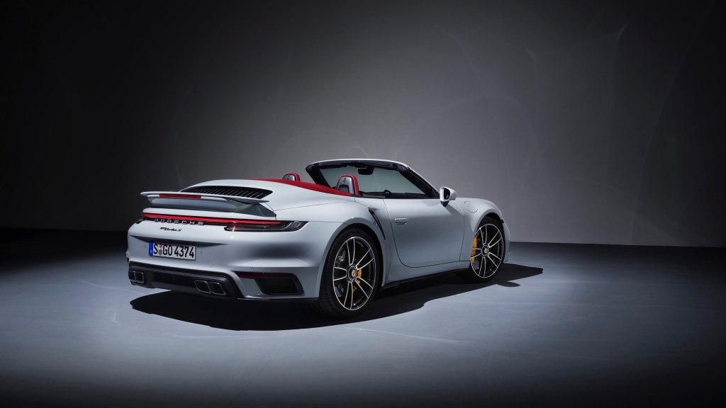 The rear 3/4 view of a white 2021 Porsche 911 Turbo S Cabriolet with its red roof down