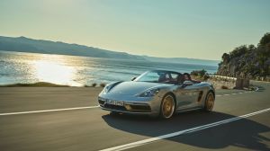 A silver 2021 Porsche Boxster 25 Years driving down a highway with a body of water behind them.