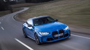 A blue 2022 BMW M4 Competition xDrive goes around a corner on a public road