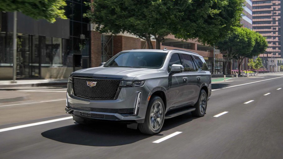 A gray 2022 Cadillac Escalade drives along a road during the day with buildings in the background.