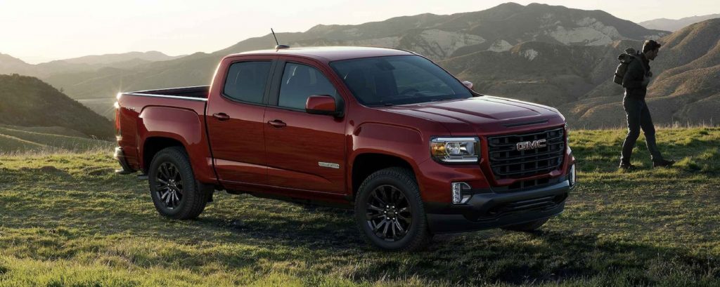 A red 2022 GMC Canyon parked in a valley with a backpacker walking by.