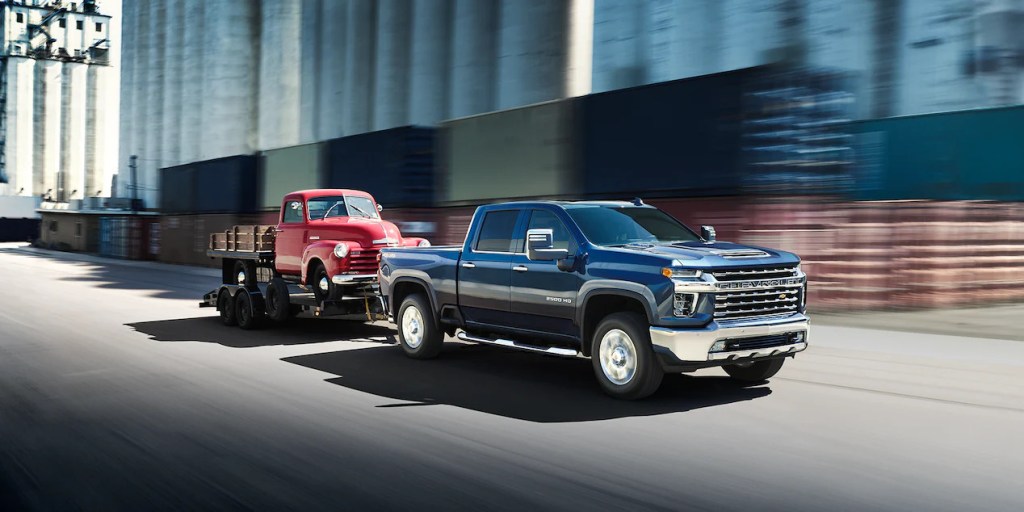 A blue 2022 Chevy Silverado 2500 HD heavy-duty pickup truck towing a trailer down the road, it's one of the most discounted new pickup trucks right now according to Consumer Reports.