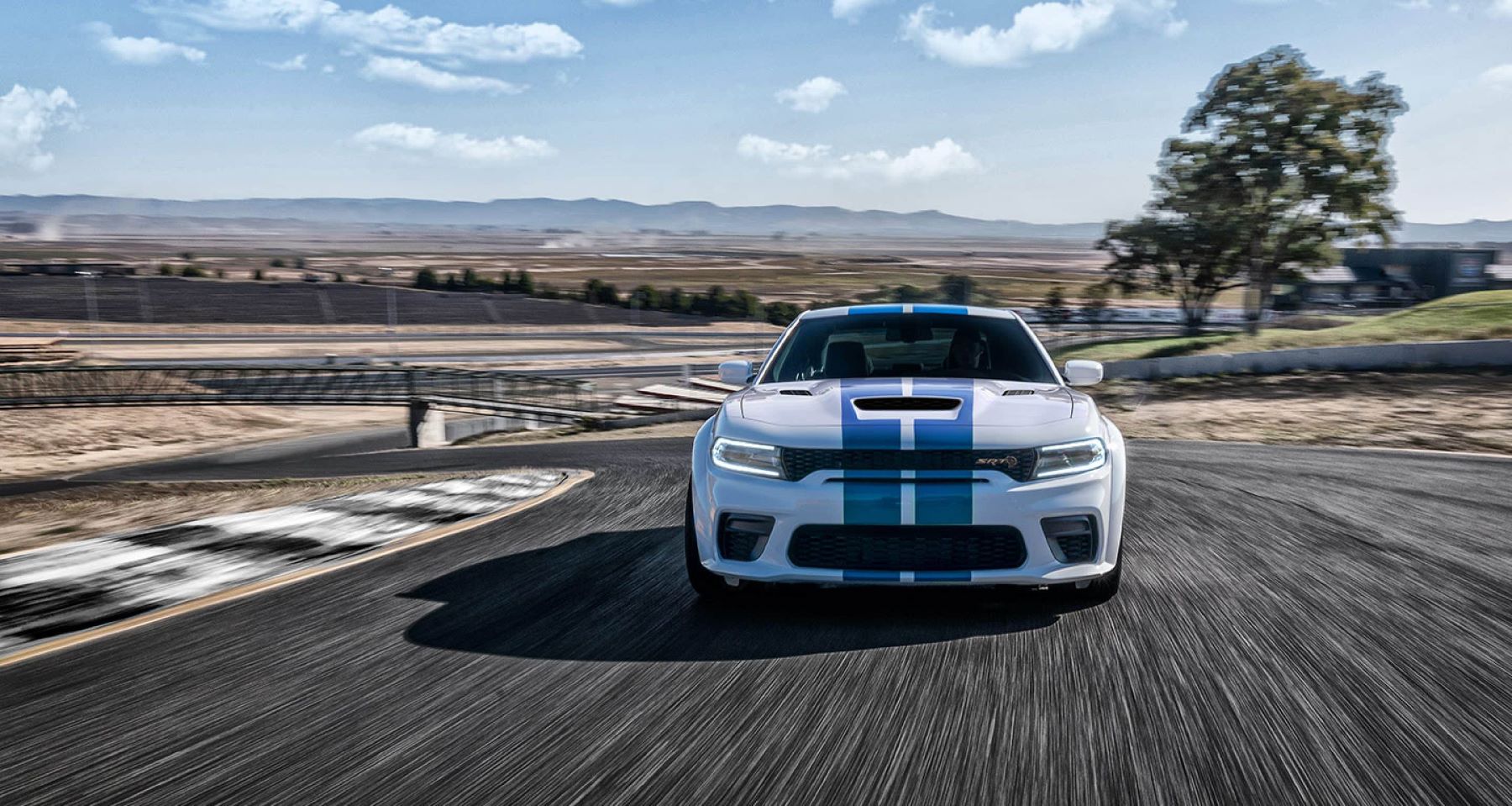 The 2022 Dodge Charger Jailbreak muscle car model with the Old Glory hood stripe paint color option driving on a race track