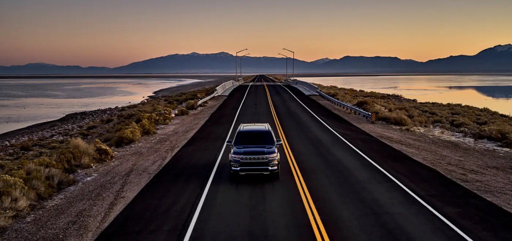 A 2022 Jeep Grand Wagoneer driving down a highway at sunset.