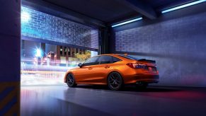 The rear 3/4 view of an orange 2022 Honda Civic Si in a garage