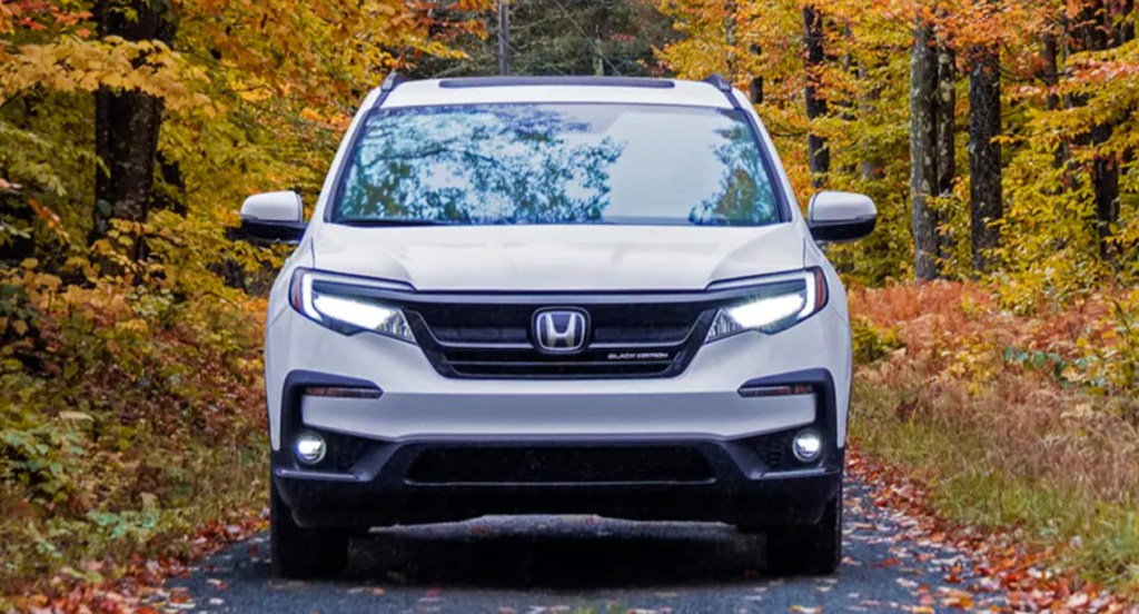 A white 2022 Honda PIlot is parked in front of a fall scene. 
