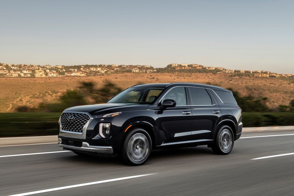 A 2022 Hyundai Palisade midsize crossover SUV driving down a highway with homes on grassy hills in the background