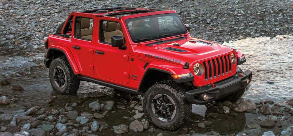 A 2022 Jeep Wrangler Rubicon compact off-road SUV with the Firecracker Red paint color option parked on a trail of water, mud, and rocks