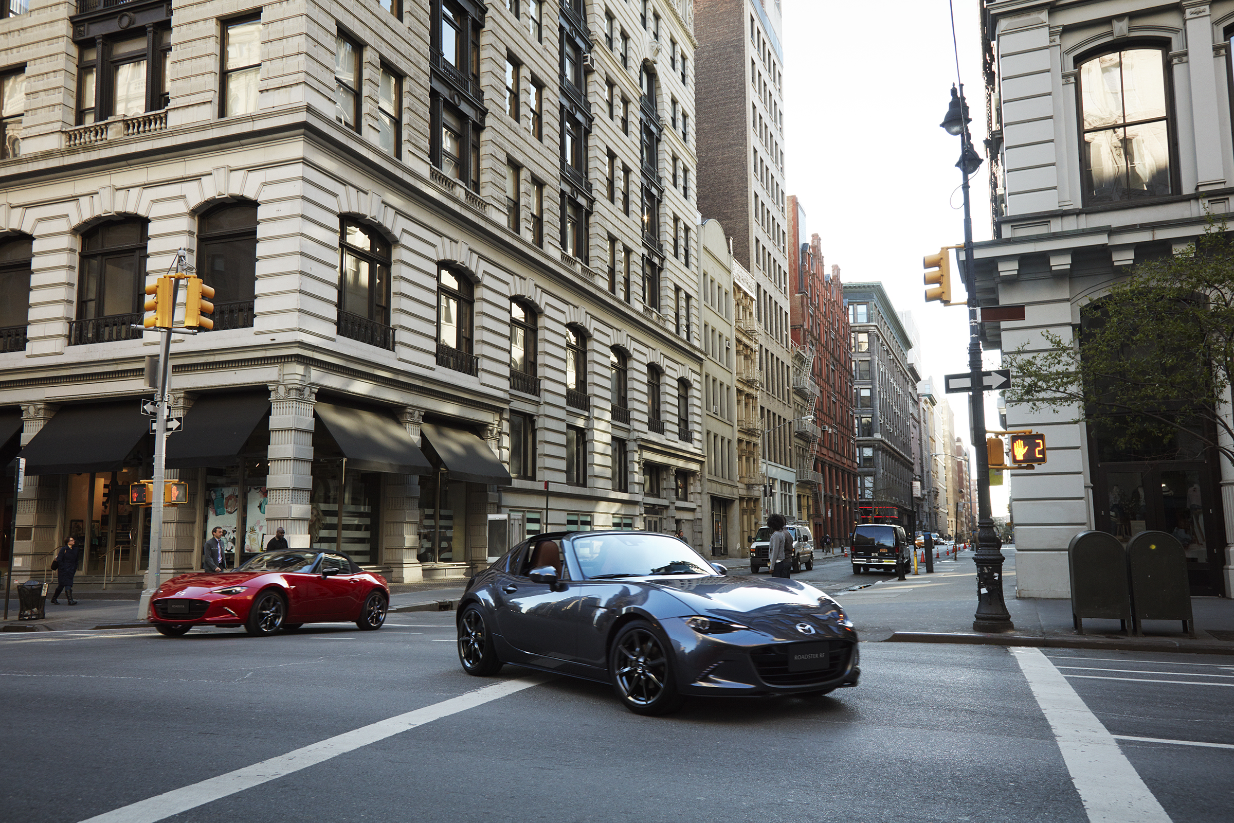 A pair of Mazda Miata sports cars shot from the 3/4 angle on a city street