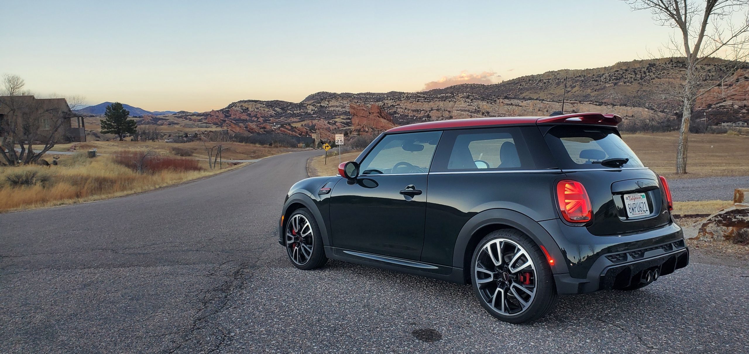A racing green 2022 Mini Cooper JCW hot hatch shot from the front rear 3/4 at dusk in the Rockies