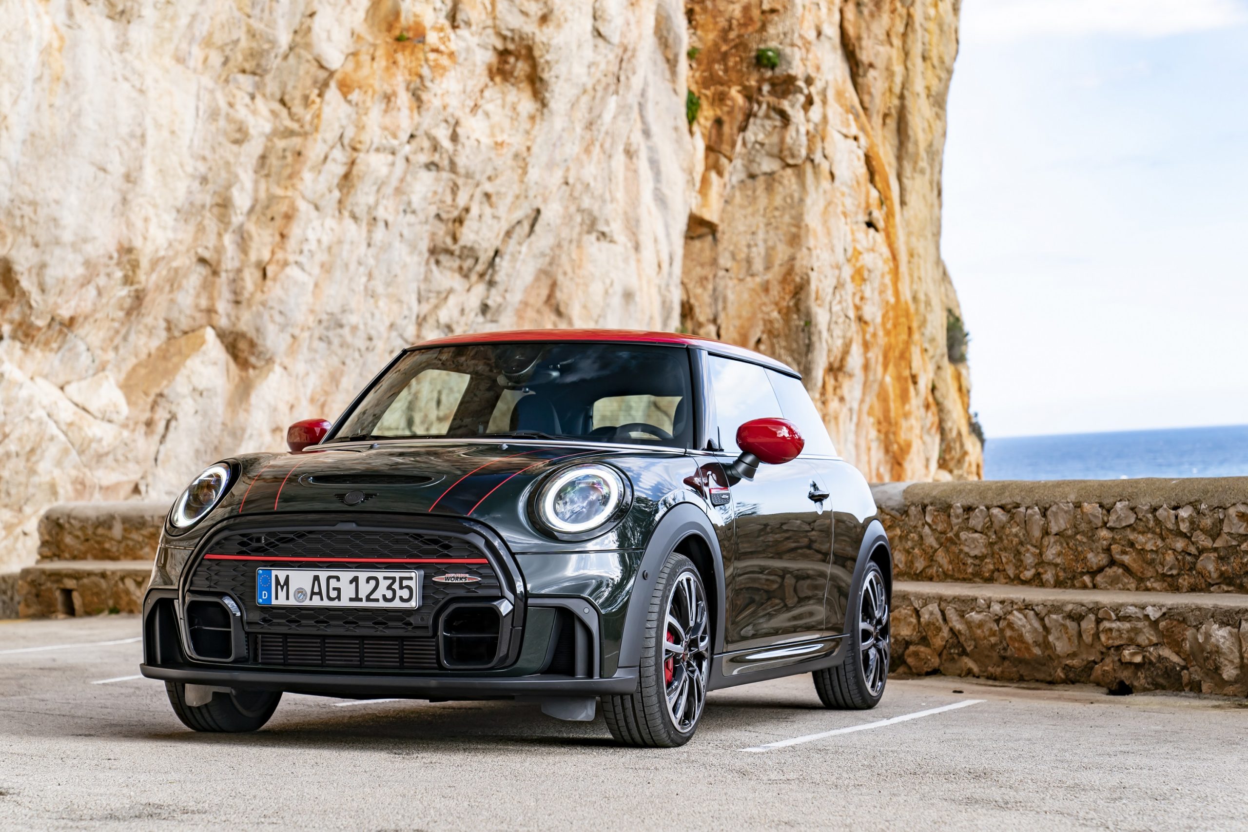 A racing green Mini Cooper JCW hatchback shot from the front 3/4 on a seaside cliff