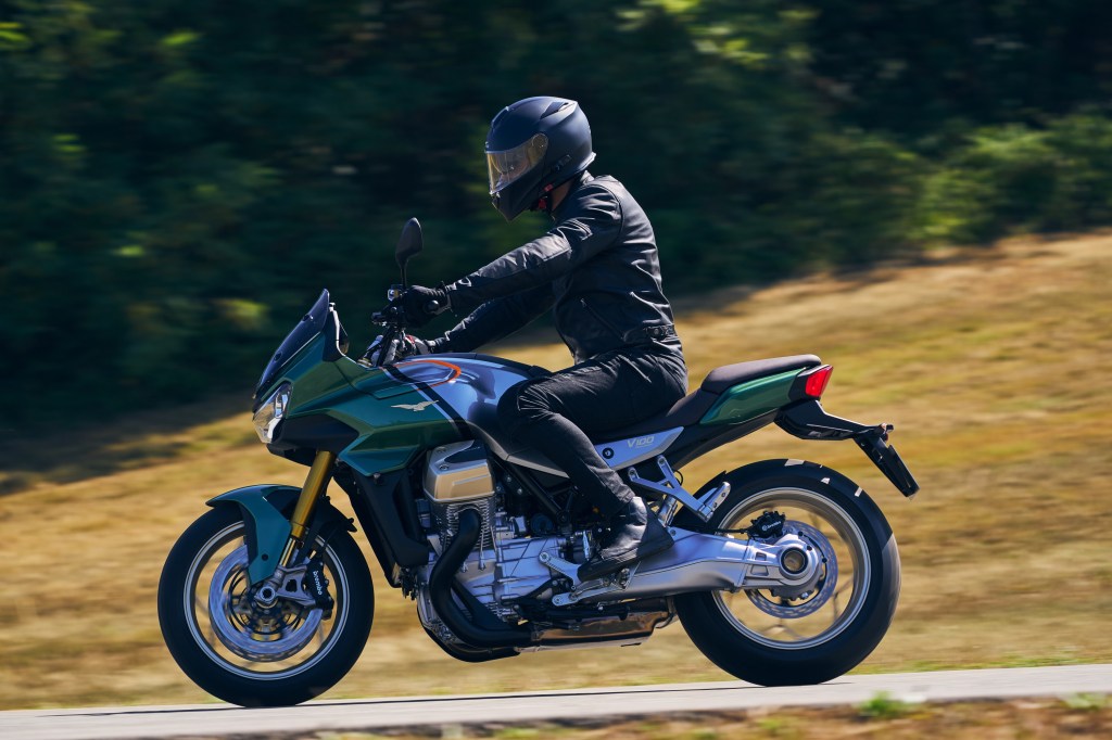 A black-clad rider on a green-and-silver 2022 Moto Guzzi V100 Mandello riding through the countryside