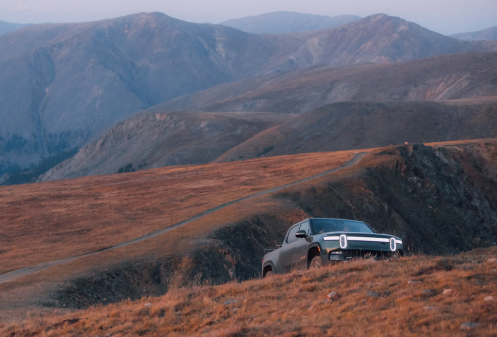 2022 Rivian R1T driving on a mountain path, highlighting the Rivian Adventure Network of EV charging stations