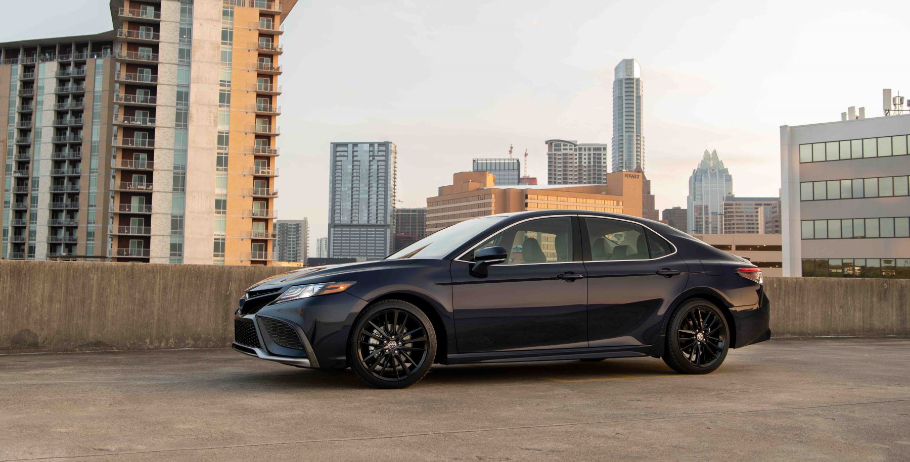 A 2022 Toyota Camry XSE midsize sedan with a black paint color option parked on the top of a roof with a skyline of skyscrapers in the background