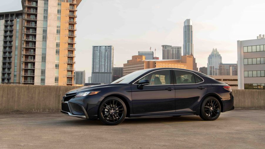 A 2022 Toyota Camry XSE midsize sedan with a black paint color option parked on the top of a roof with a skyline of skyscrapers in the background