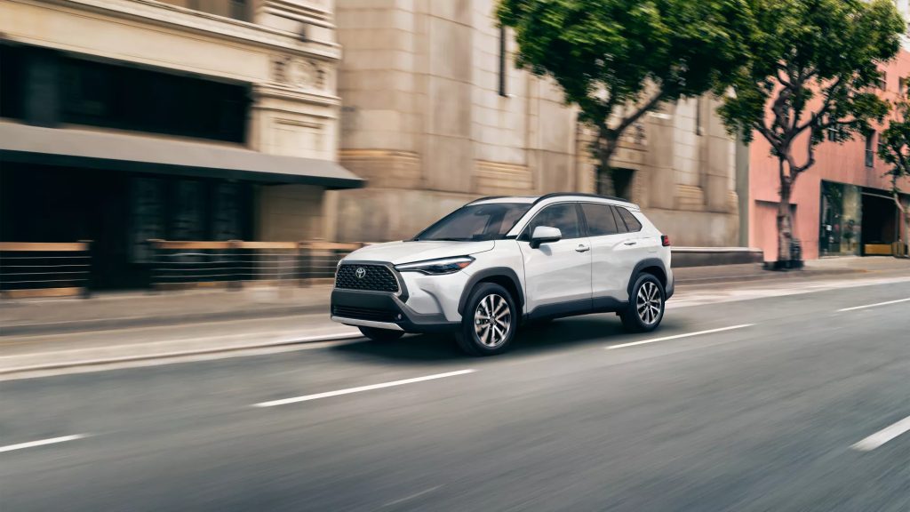 A white 2022 Toyota Corolla Cross driving, the compact crossover SUV crushes the 2022 Nissan Rogue Sport, according to KBB.