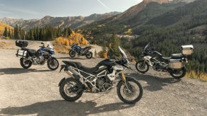 Accessorized and stock 2022 Triumph Tiger 1200 blue-and-gray GT and green-and-white Rally Pros on a mountain