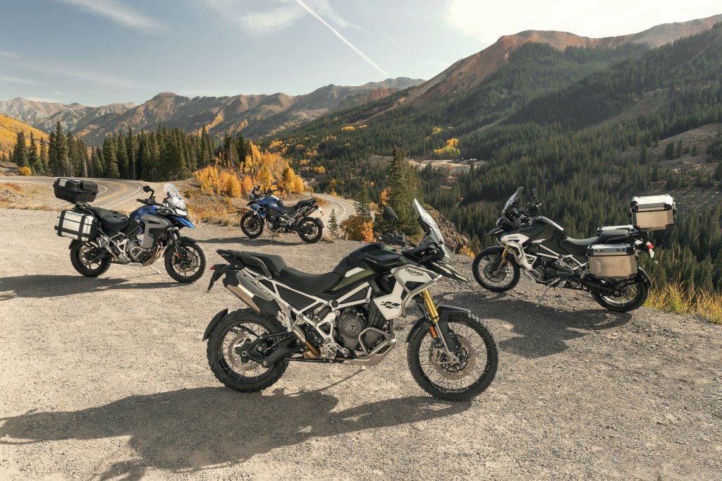 Accessorized and stock 2022 Triumph Tiger 1200 blue-and-gray GT and green-and-white Rally Pros on a mountain