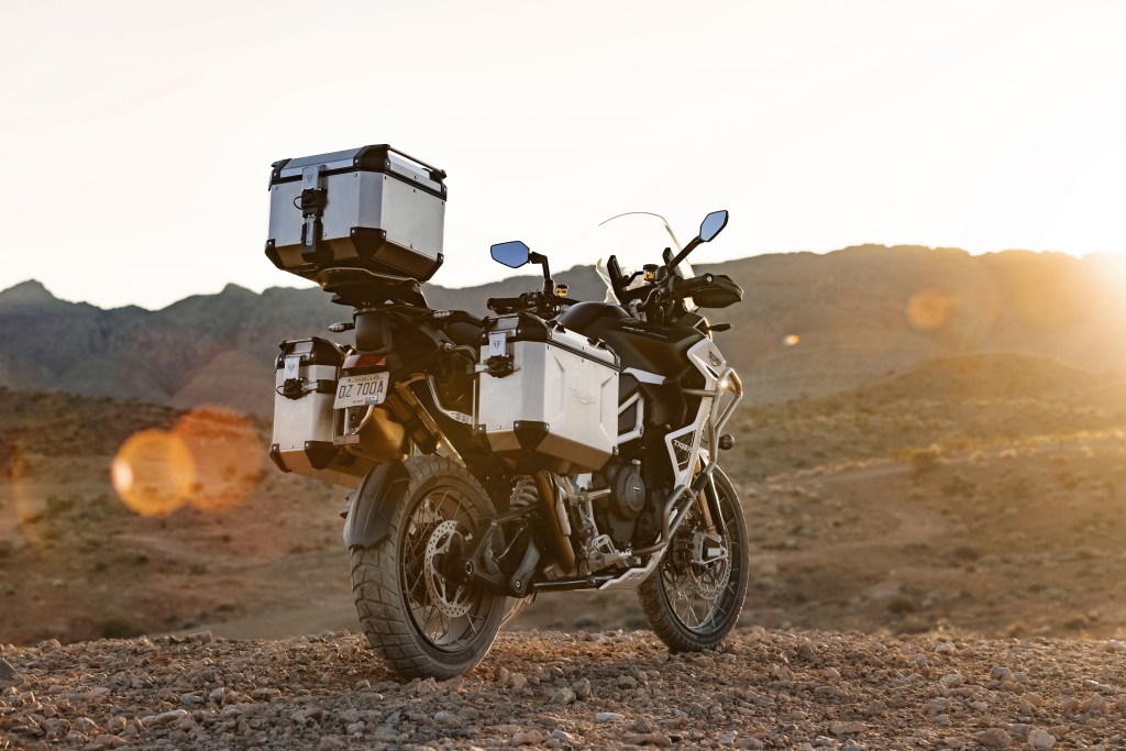 The rear 3/4 view of a black-and-white 2022 Triumph Tiger 1200 Rally Explorer with accessories in the desert