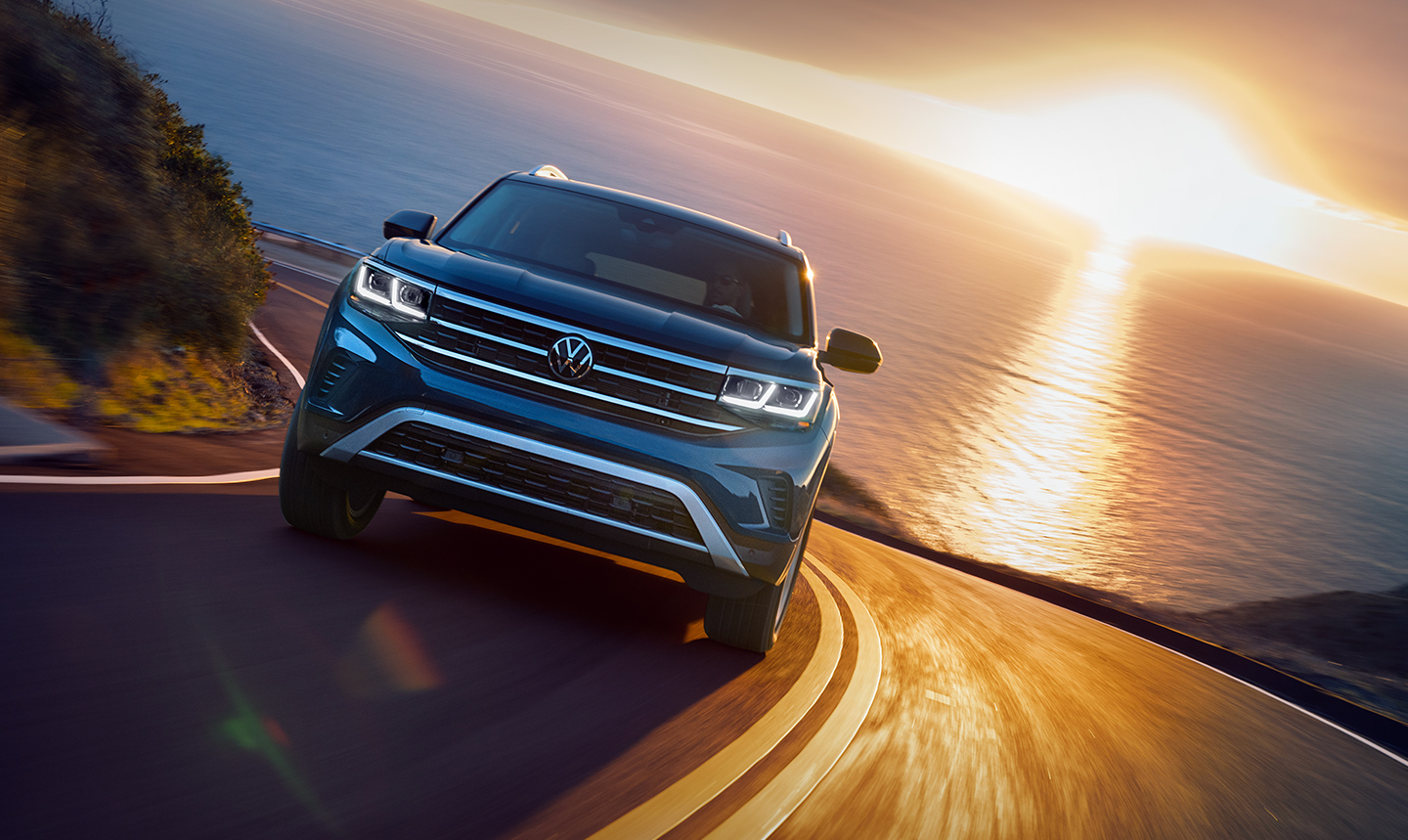 A blue 2022 Volkswagen Atlas drives on a winding road during a sunset in the background, how much does a fully loaded one cost?