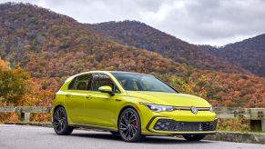 A 2022 Volkswagen Golf GTI hot hatch with a bright yellow paint color option parked near a forest of autumn trees