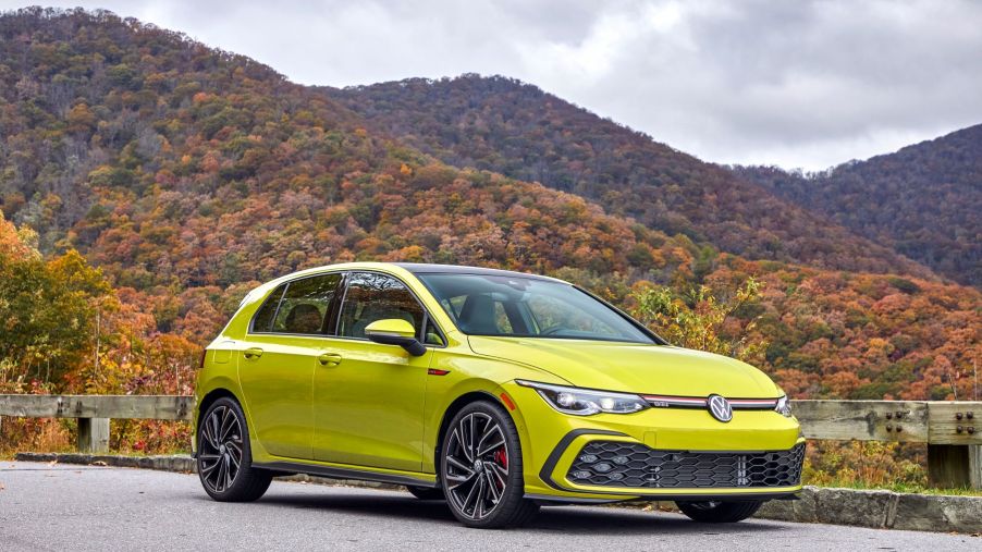 A 2022 Volkswagen Golf GTI hot hatch with a bright yellow paint color option parked near a forest of autumn trees