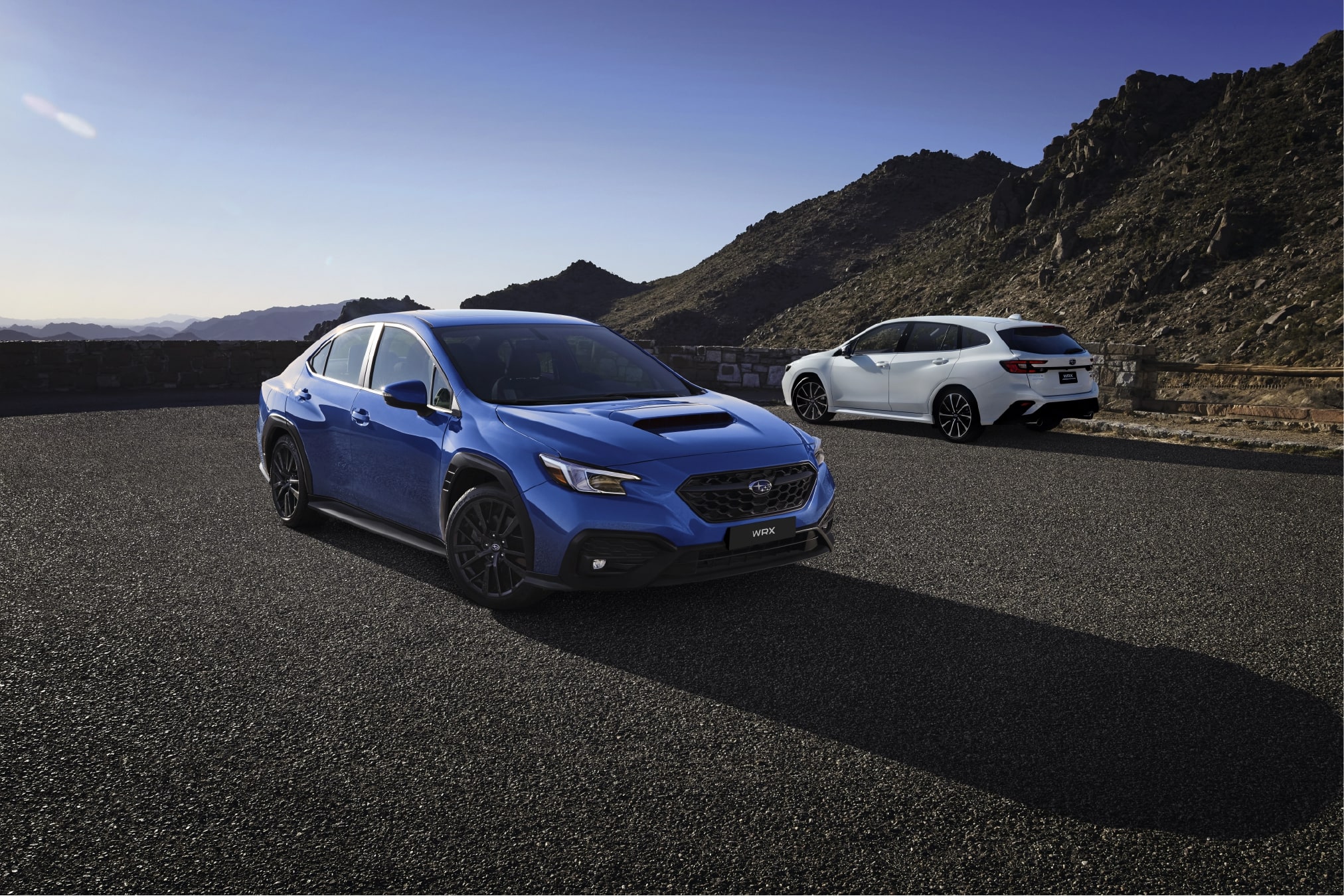 A 2022 WRX sedan in blue and a white Sportwagon on a highway turnout