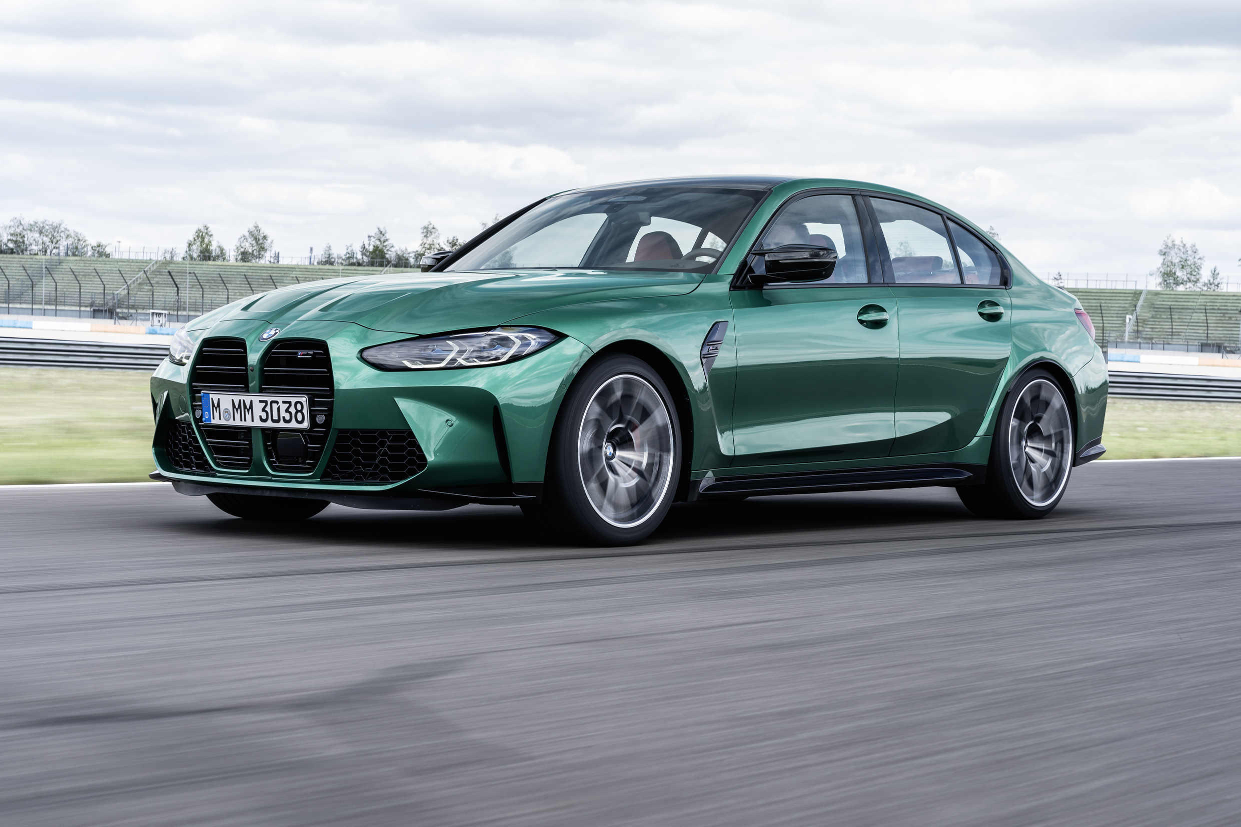An emerald green 2022 BMW M3 sedan shot from the front 3/4 angle on a race track