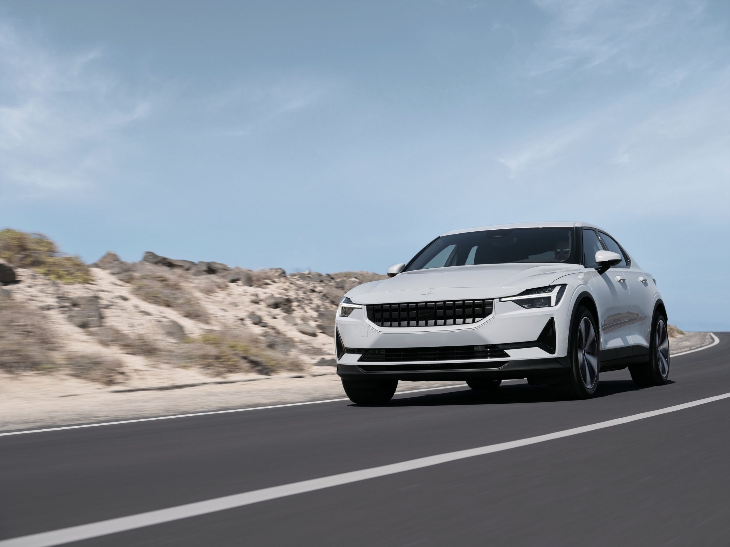 A white Polestar 2 EV shot from the front 3/4 on a beach road