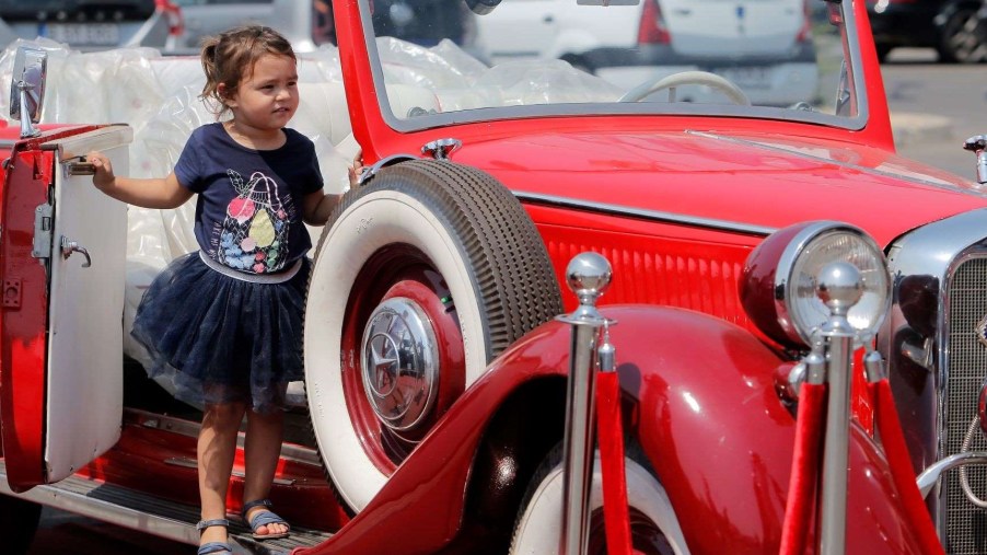 A child standing by the door of an antique, car, thinking about a car book for kids Christmas gift