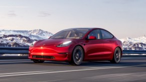 A fully loaded new Red Multi-Coat 2022 Tesla Model 3 driving by snowy mountains