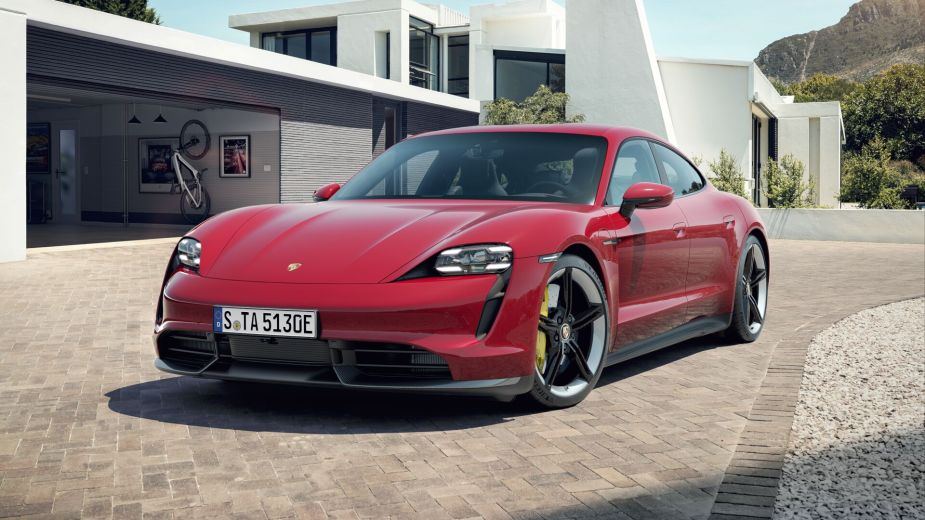 A fully loaded new Carmine Red 2022 Porsche Taycan Turbo S parked near a modern house