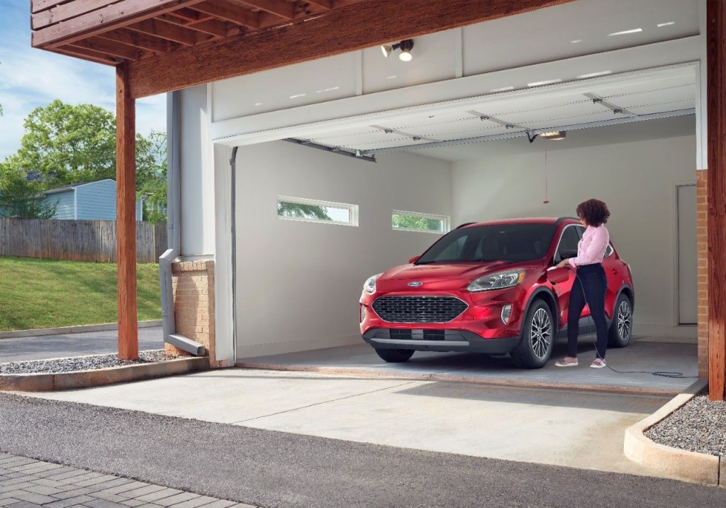 A woman charging a red 2022 Ford Escape PHEV, a plug-in hybrid to save money on gas