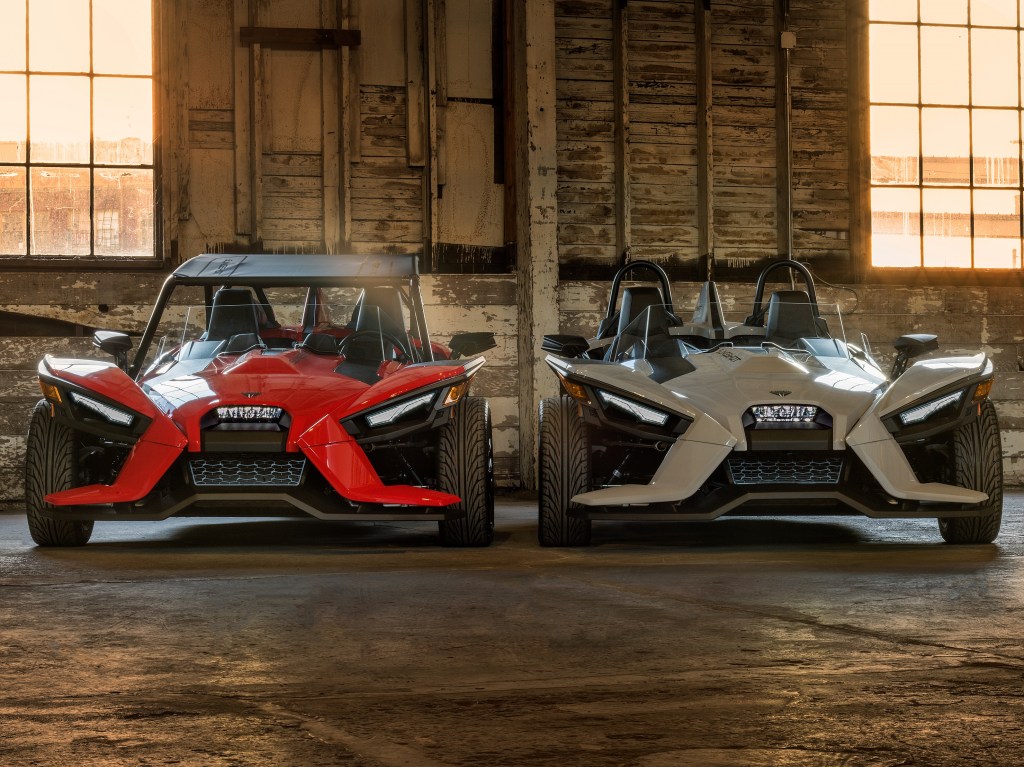 A red accessorized 2022 Polaris Slingshot S next to a white standard one in a garage