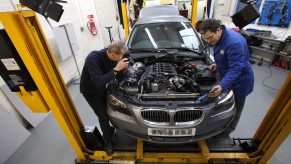Two men work on a BMW sedan in a shop