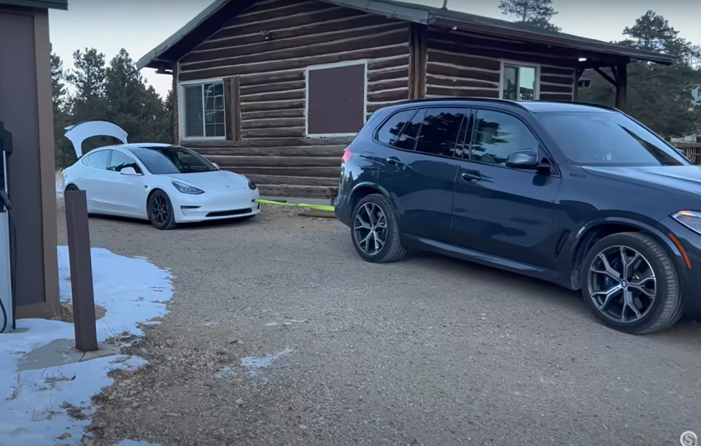 BMW X5 PHEV getting ready to tow charge a Tesla Model 3 by a log cabin in Colorado