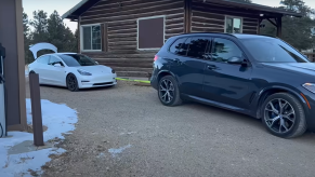 BMW X5 PHEV getting ready to tow charge a Tesla Model 3 by a log cabin in Colorado