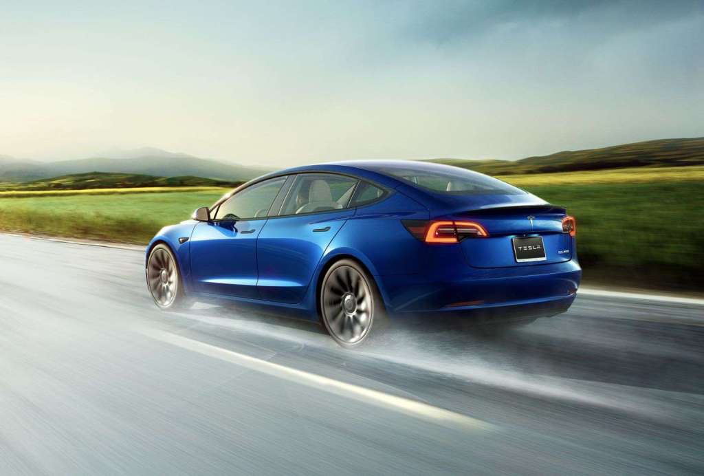 Blue 2022 Tesla Model 3 driving on a road in rainy weather