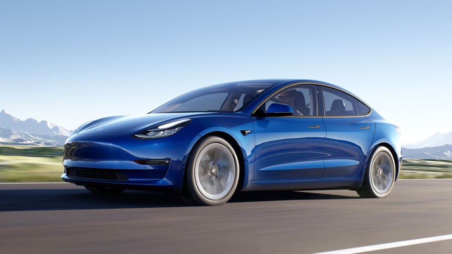 Blue 2022 Tesla Model 3, which costs less own than a gas car, driving by mountains