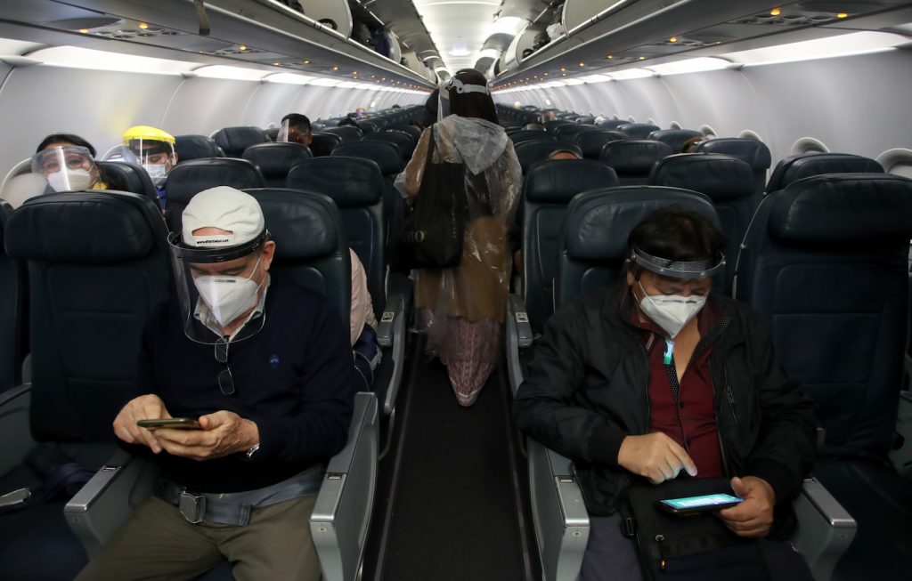 Masked travelers on an airplane must keep track of COVID-19 travel restrictions | Raul Sifuentes via Getty Images