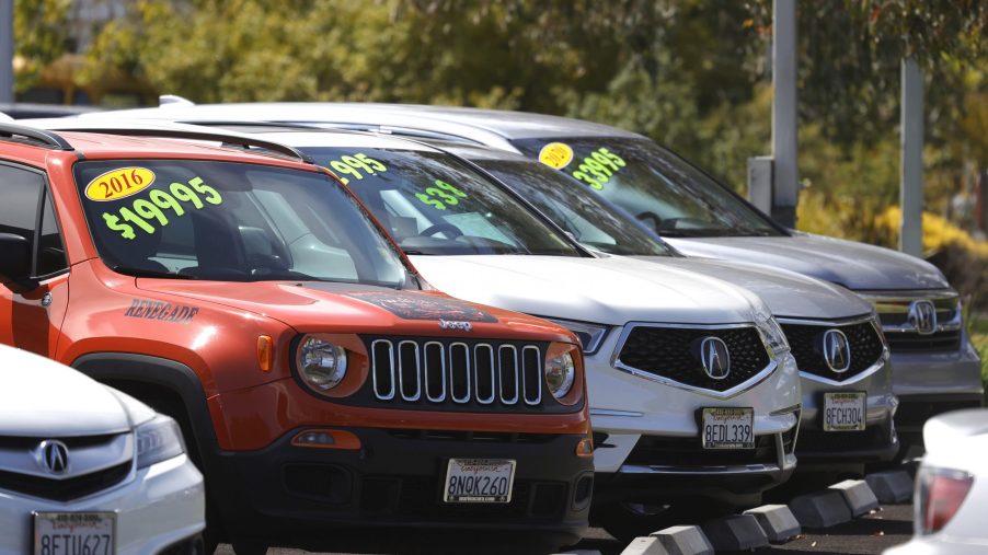 A selection of new and used cars with prices on their windshields at a dealer