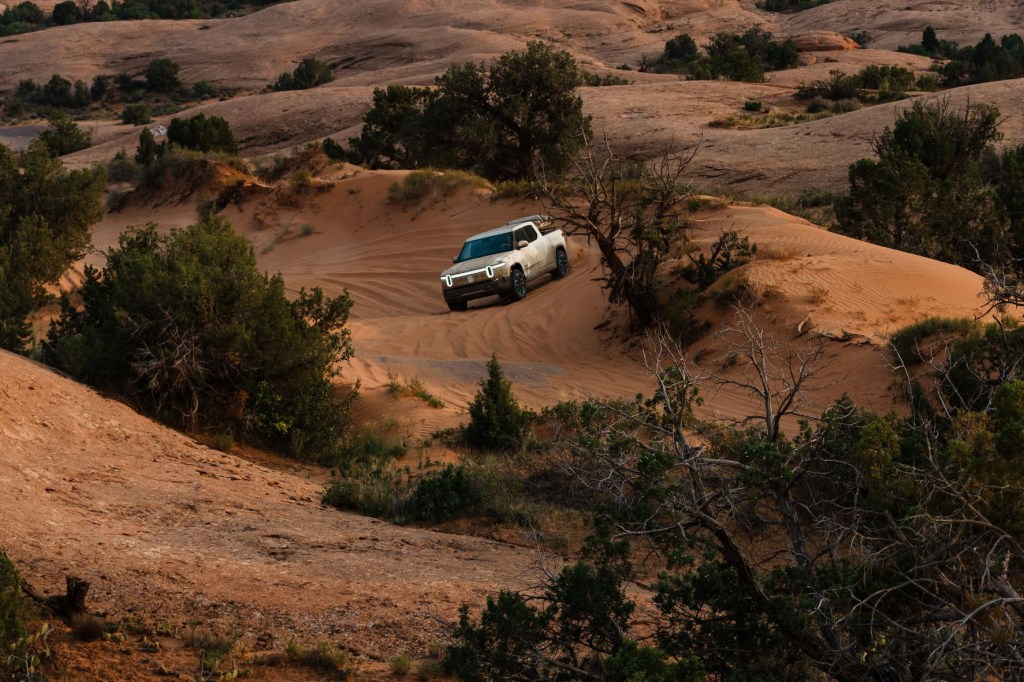 Glacier White 2022 Rivian R1T driving off-road on sandy terrain