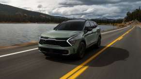 Green 2023 Kia Sportage driving by a mountain lake
