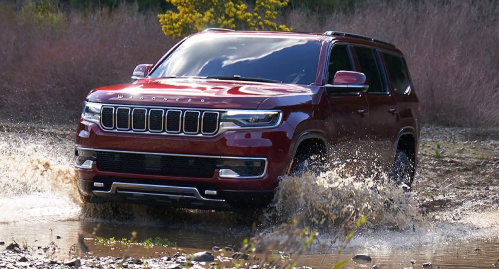 A red Jeep Wagoneer is driving through water off-road. 